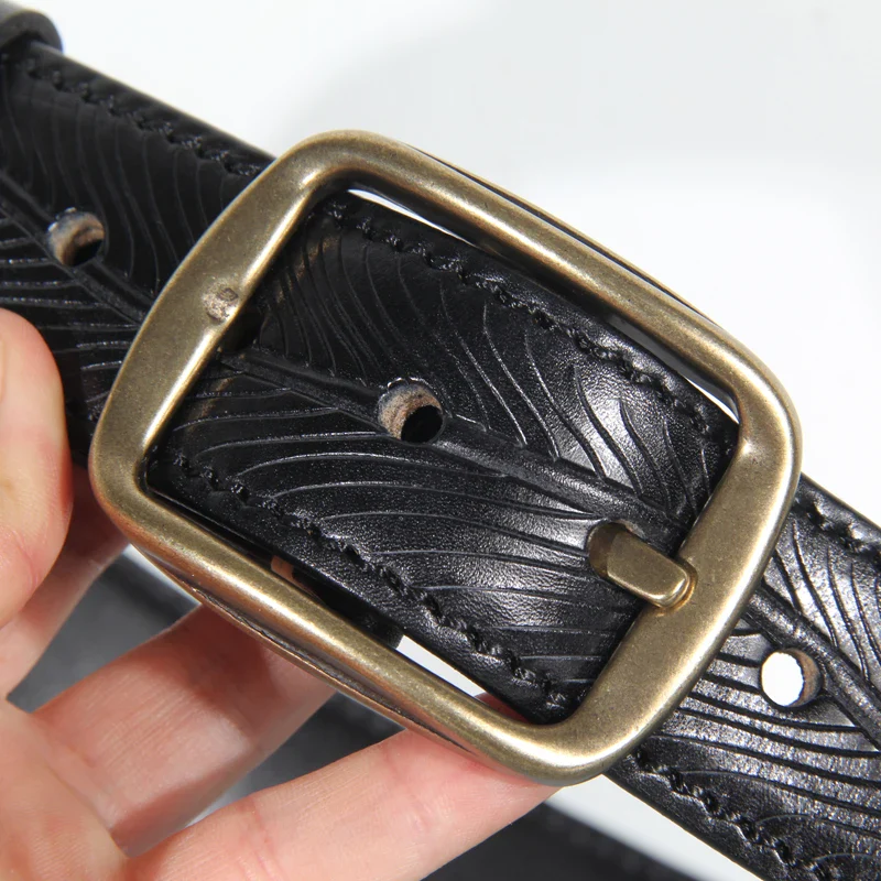 Leather belt with embossed double-sided heritage design and brass buckle. Embossed leather belt with brass buckle, featuring double-sided heritage pattern.