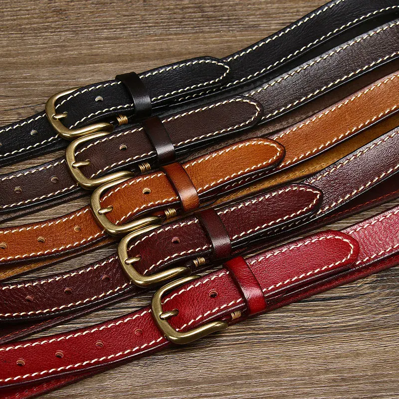 Leather belt collection in various colors on wooden surface. Leather belts in black, brown, tan, burgundy, and red with brass buckles.