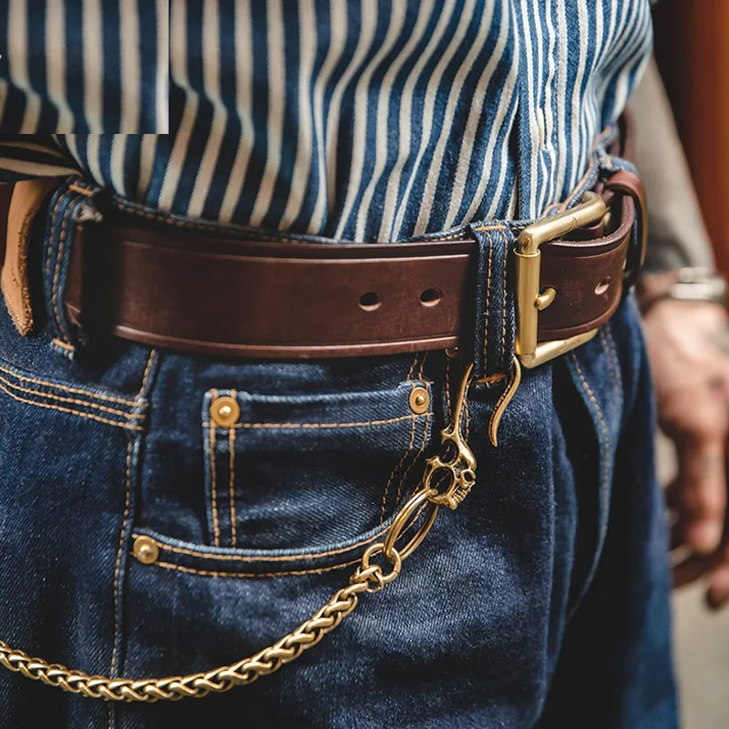 Leather belt with chain accessory on denim jeans and striped shirt. Stylish men's fashion accessory featuring a brown leather belt with a gold chain detail.