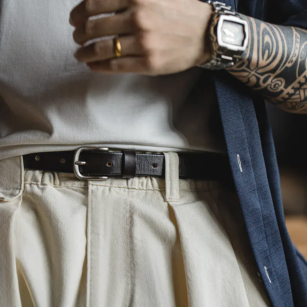 Close-up of a black leather belt worn with beige trousers and a white shirt.